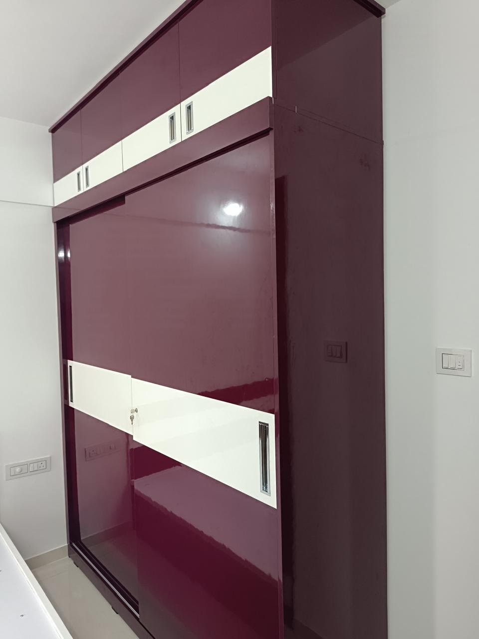 Sliding-door wardrobe in gloss maroon and white with matching loft cabinets above
