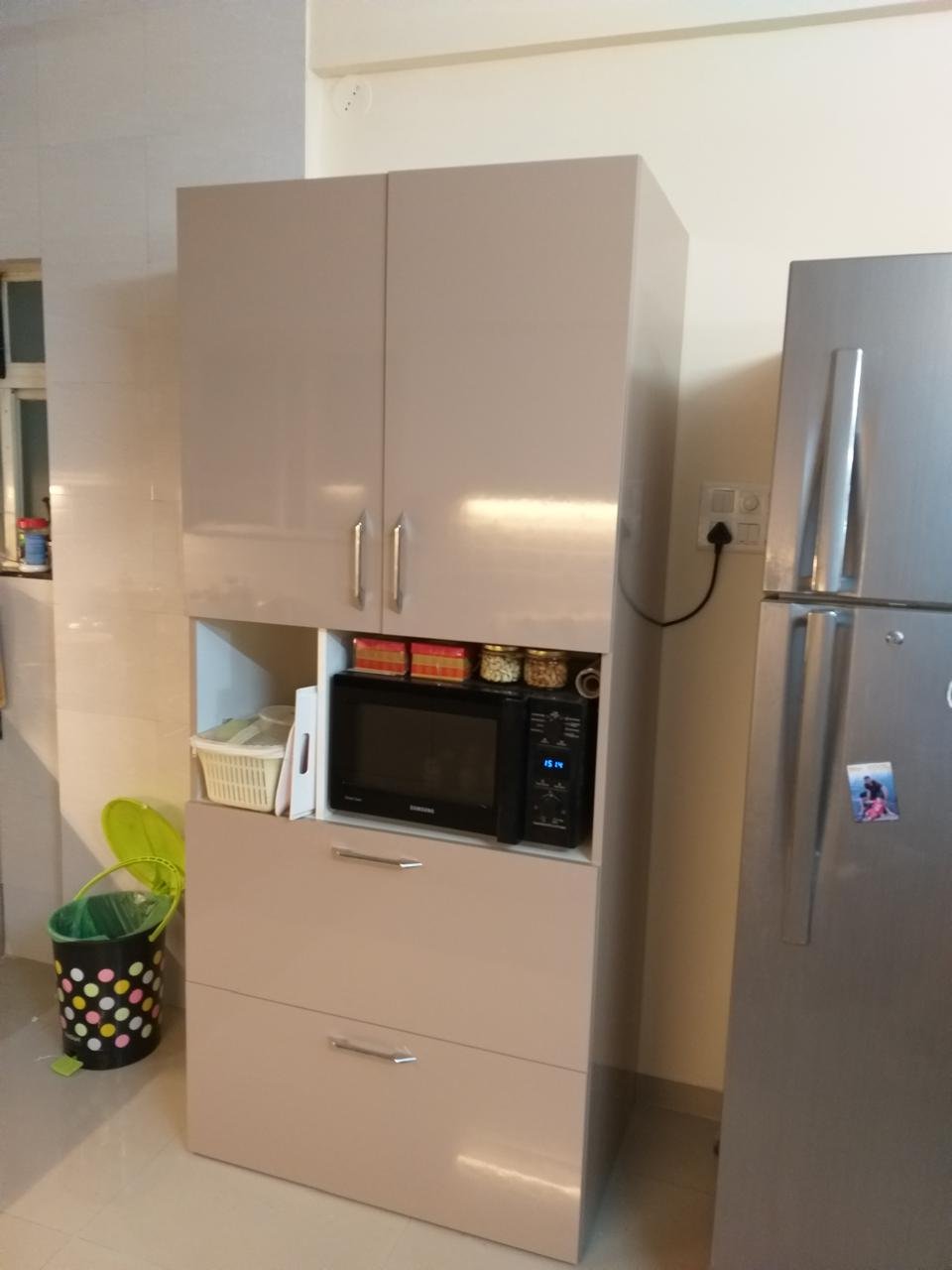 Tall kitchen cabinet in glossy beige with a built-in microwave beside a refrigerator
