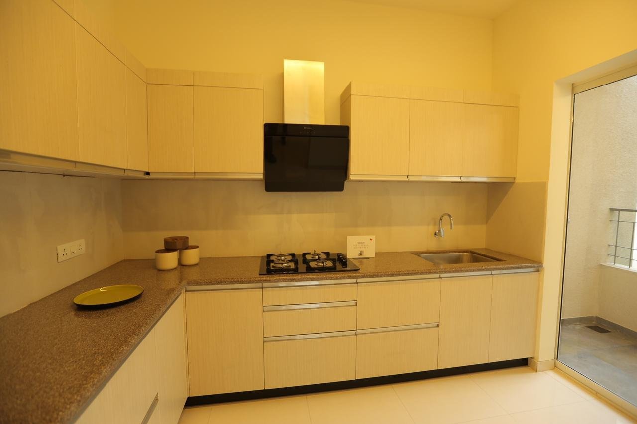 L-shaped modular kitchen in warm wood finish with a black chimney hood