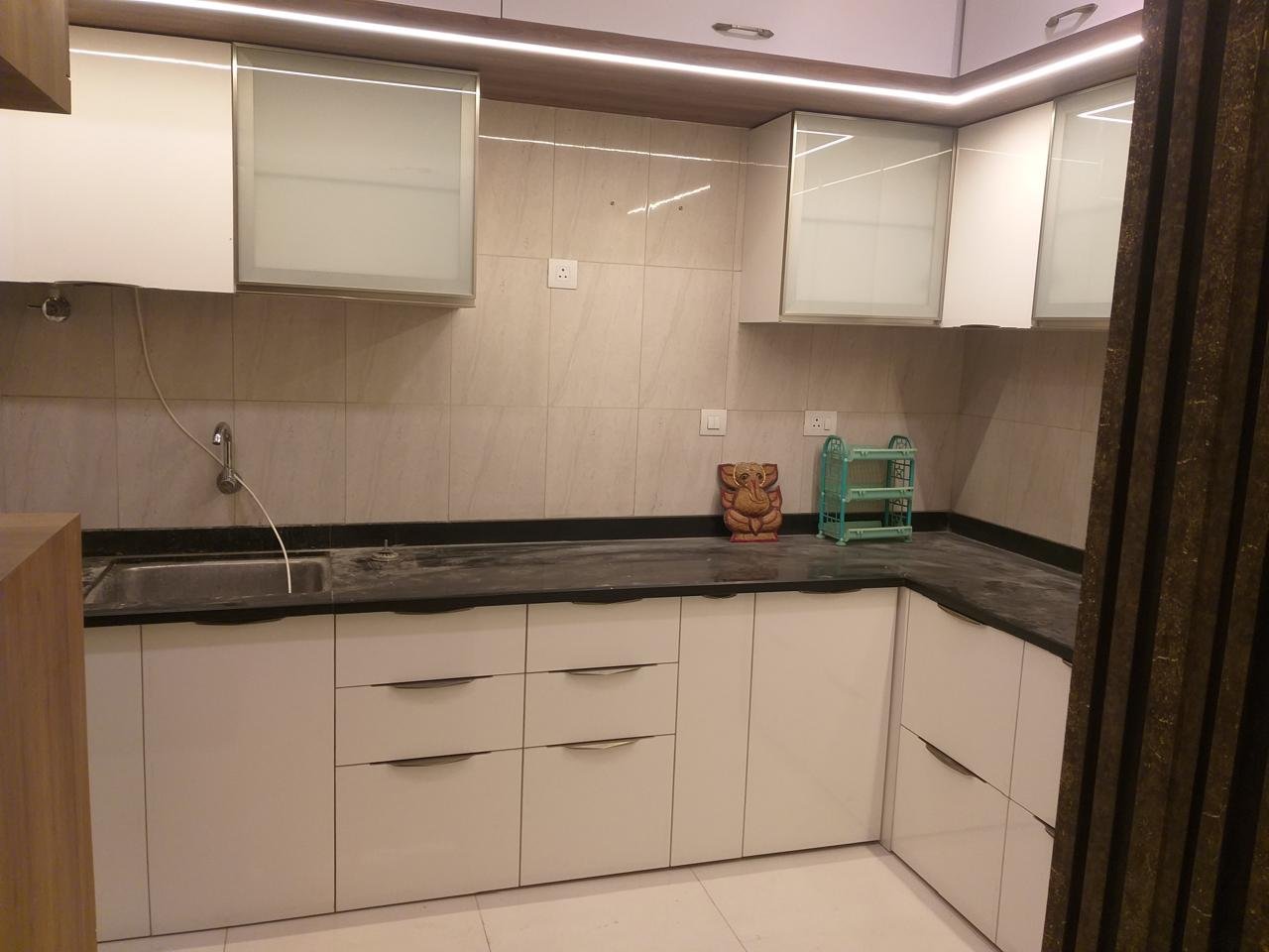 L-shaped modular kitchen in white with frosted-glass wall cabinets and a black countertop