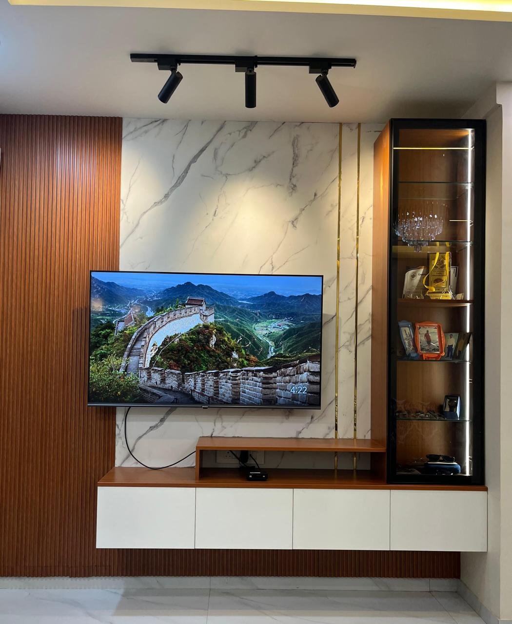 Living room media wall with a marble-finish accent panel, wood-fluted panelling and a lit glass display cabinet