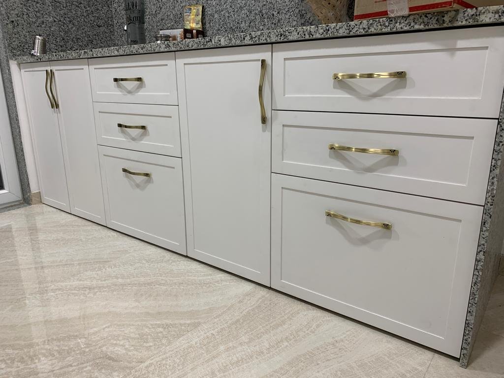 Kitchen base units in white with brass handles beneath a granite countertop